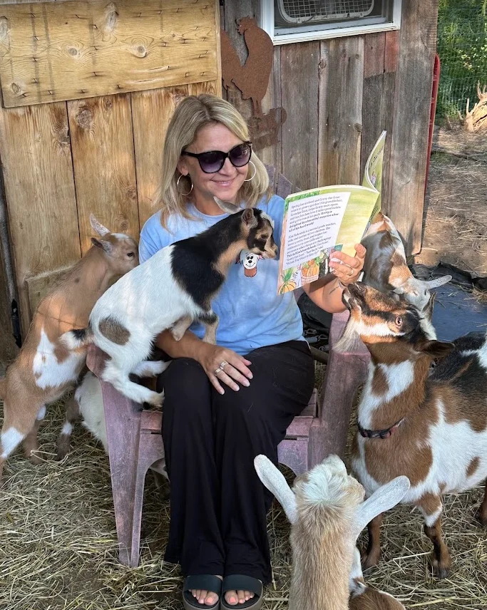 Kim Rekowski reading one of her books to a group of goats